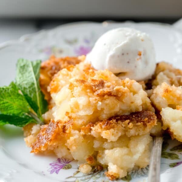pineapple dump cake on a floral gold-lined dessert plate with a spoon and ice cream scoop on top
