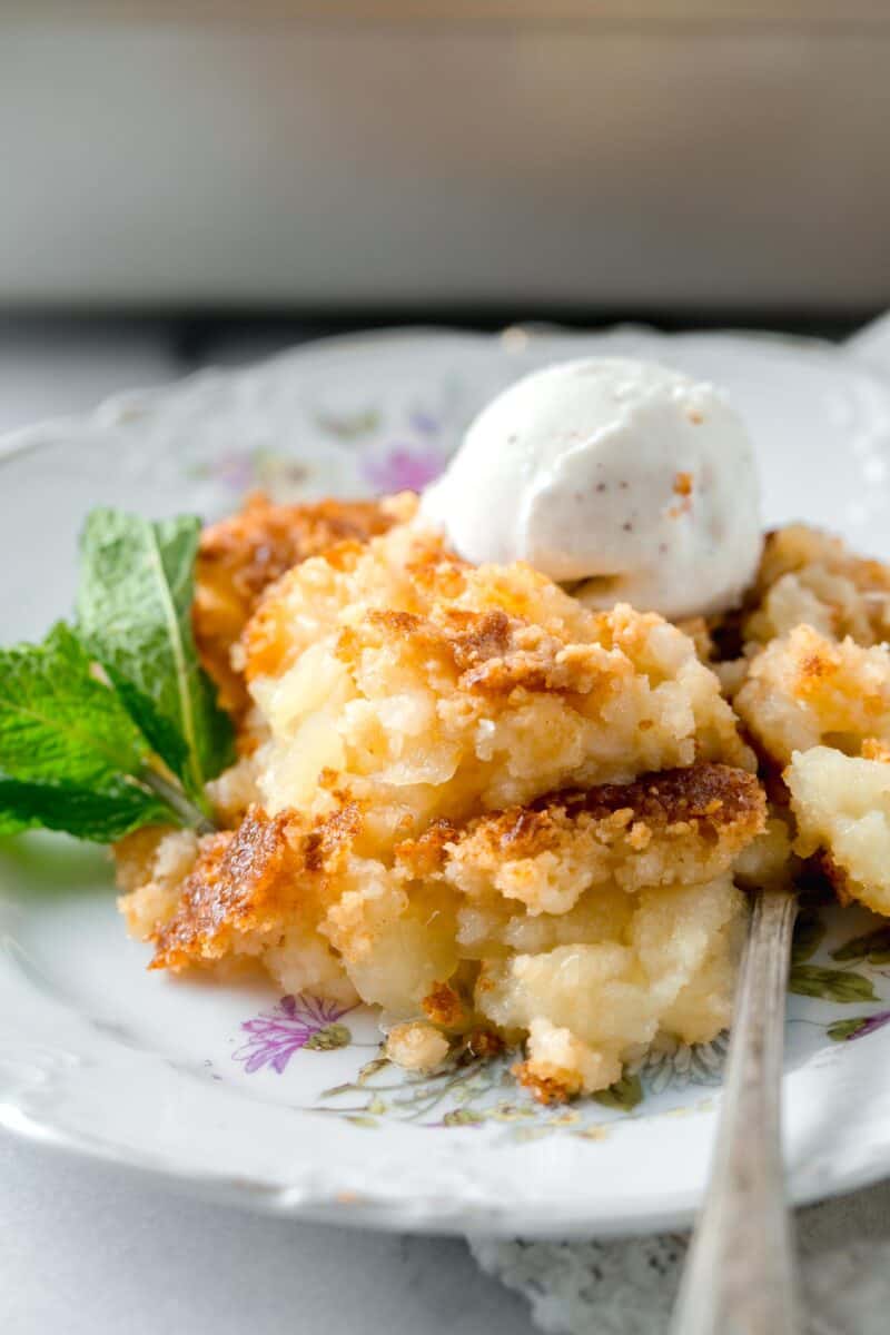 pineapple dump cake on a floral gold-lined dessert plate with a spoon and ice cream scoop on top