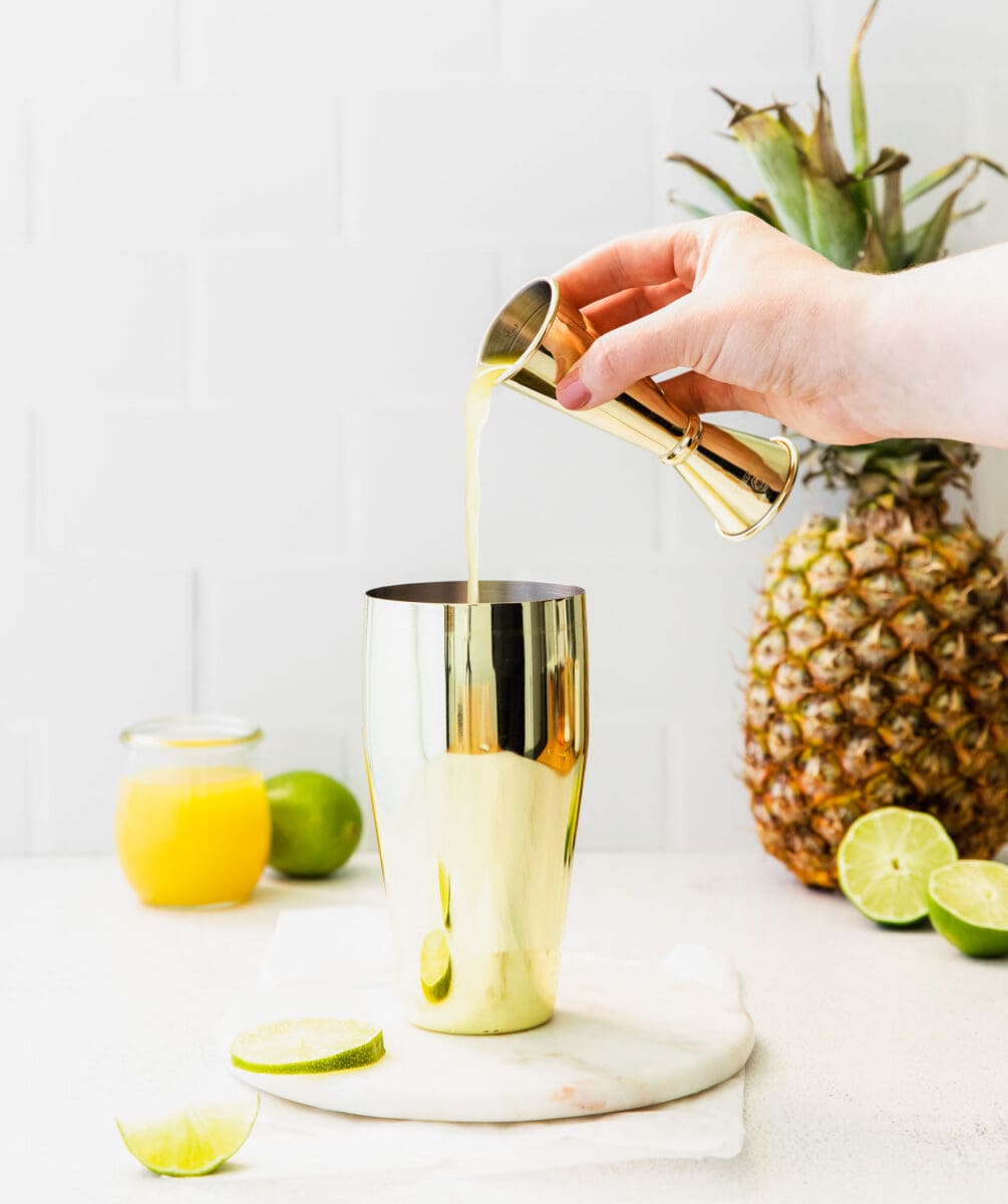 pineapple juice is being poured into a cocktail shaker
