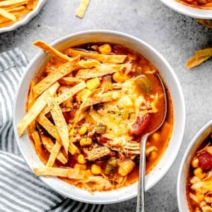 slow cooker chicken tortilla soup in a white bowl with tortilla strips and melted cheese on top