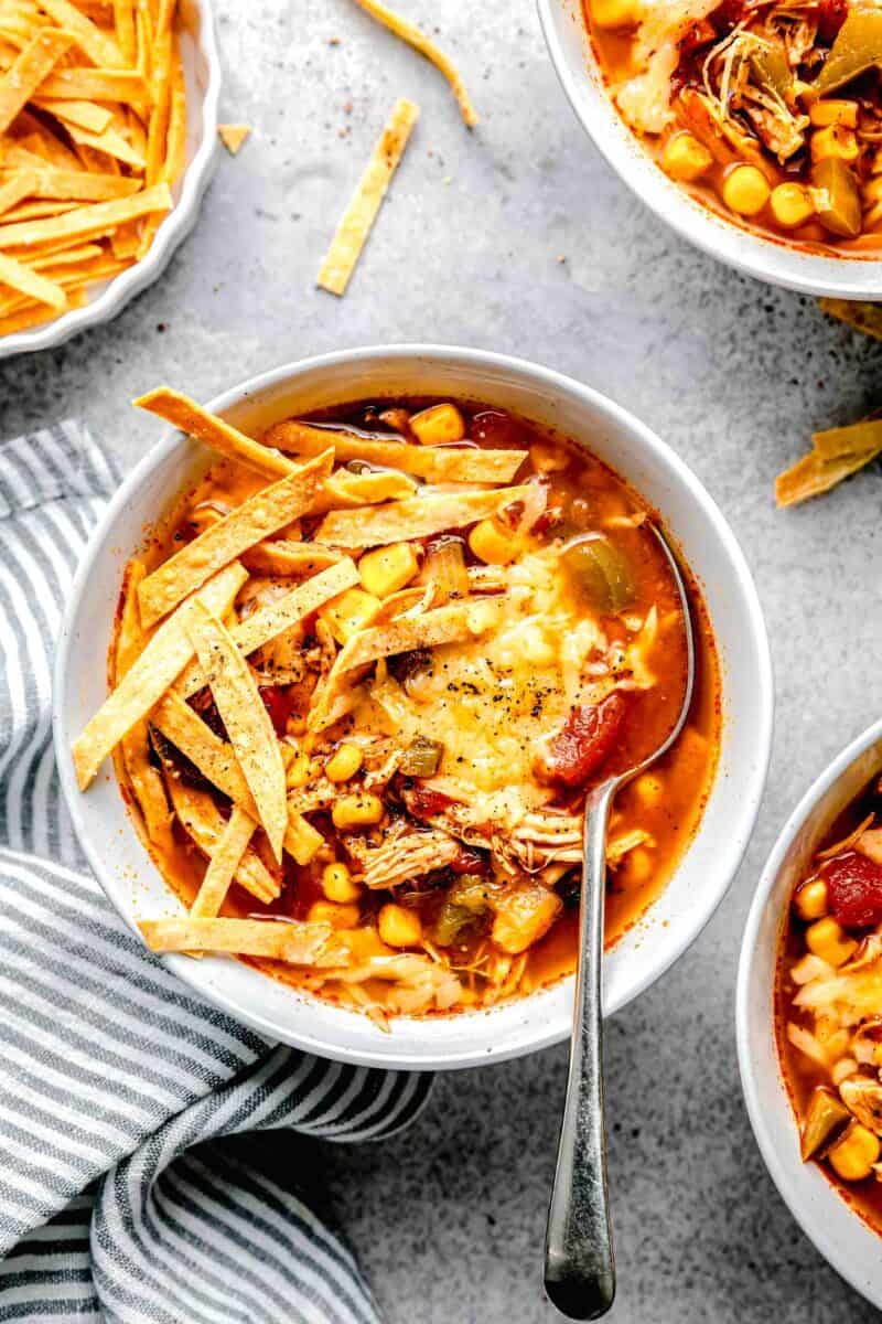 slow cooker chicken tortilla soup in a white bowl with tortilla strips and melted cheese on top