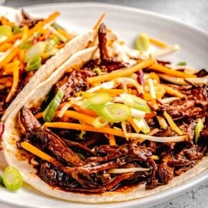 a white plate is topped with two Korean pork tacos.