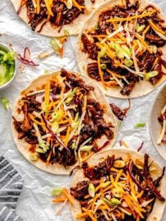 four tortillas are topped with pork and coleslaw.