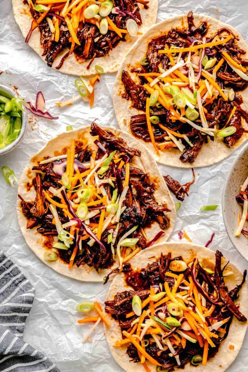 four tortillas are topped with pork and coleslaw.