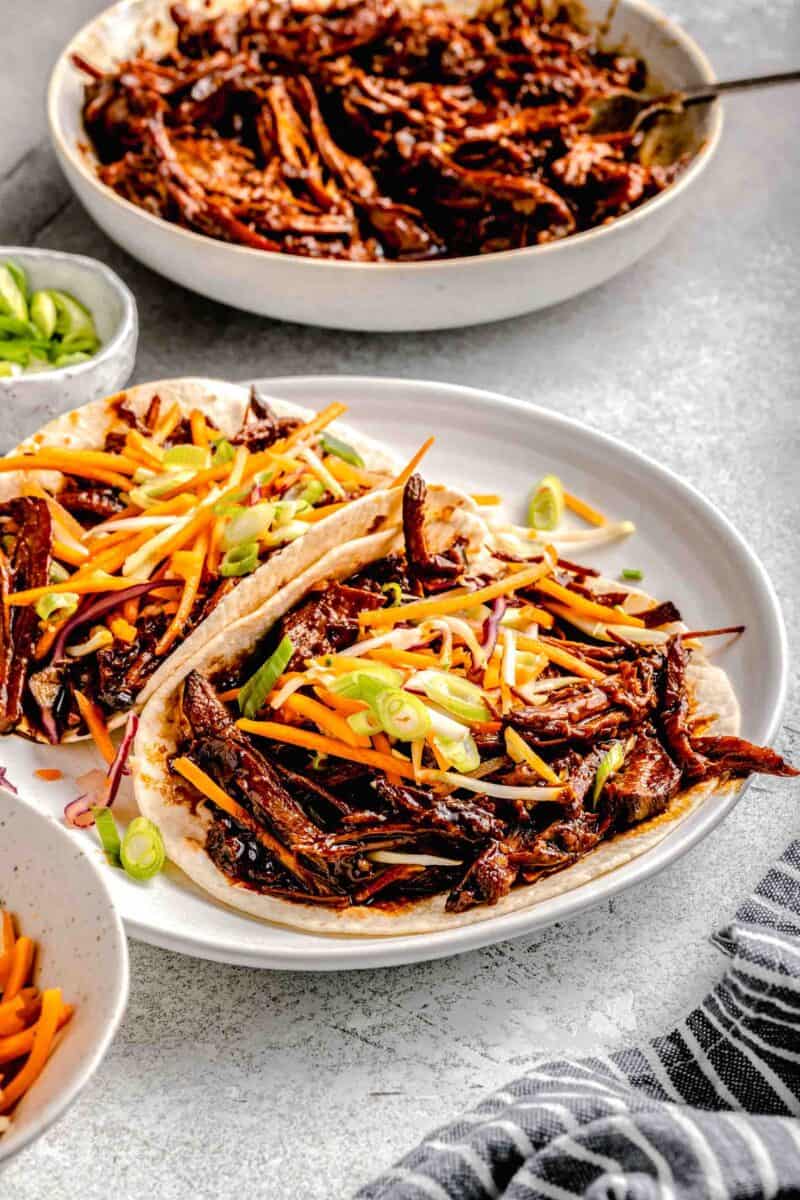 two plated tacos are topped with fresh slaw.