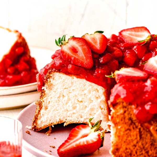 Strawberry angel food cake topped with fresh strawberries with a slice taken out of it.