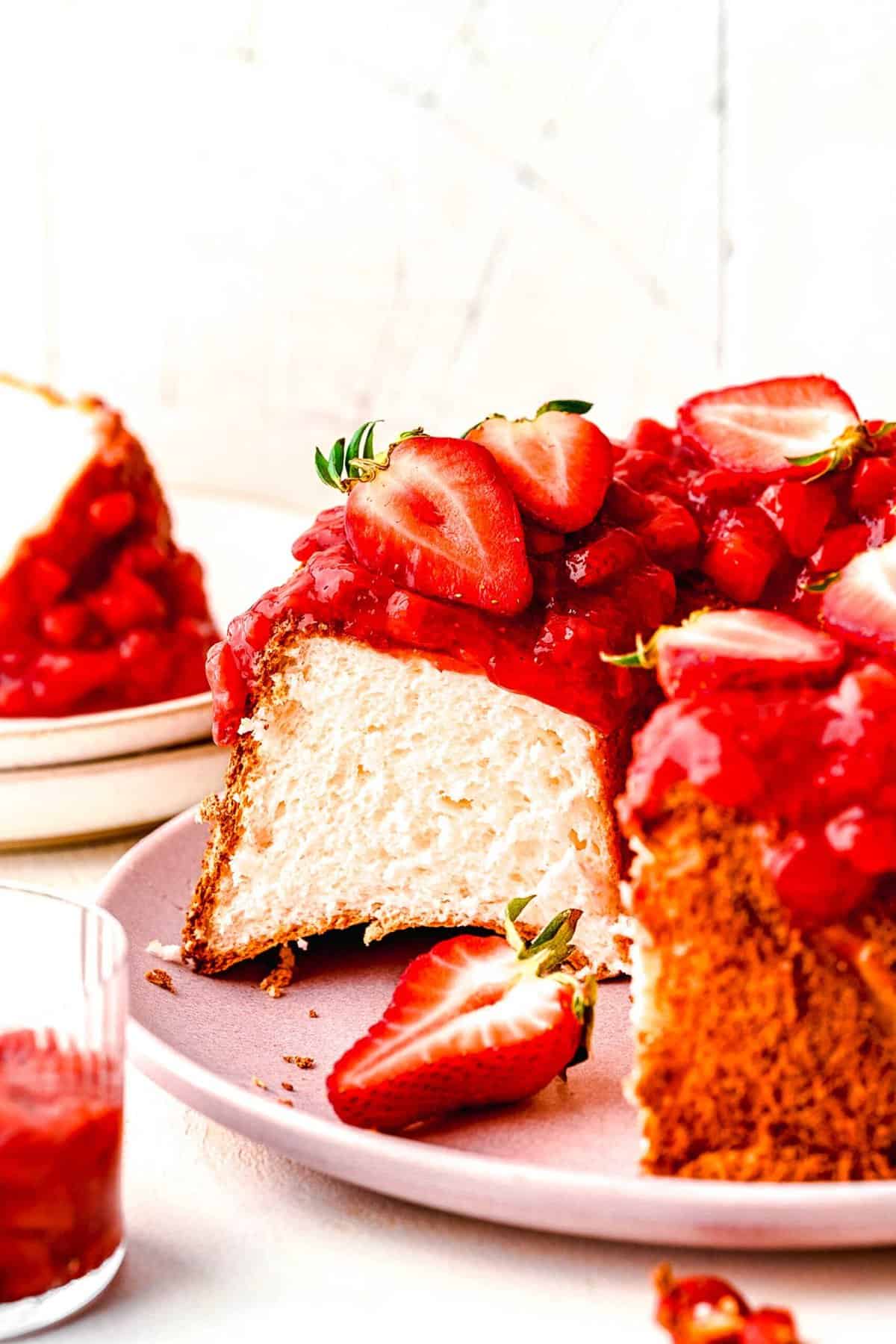 Strawberry angel food cake topped with fresh strawberries with a slice taken out of it.