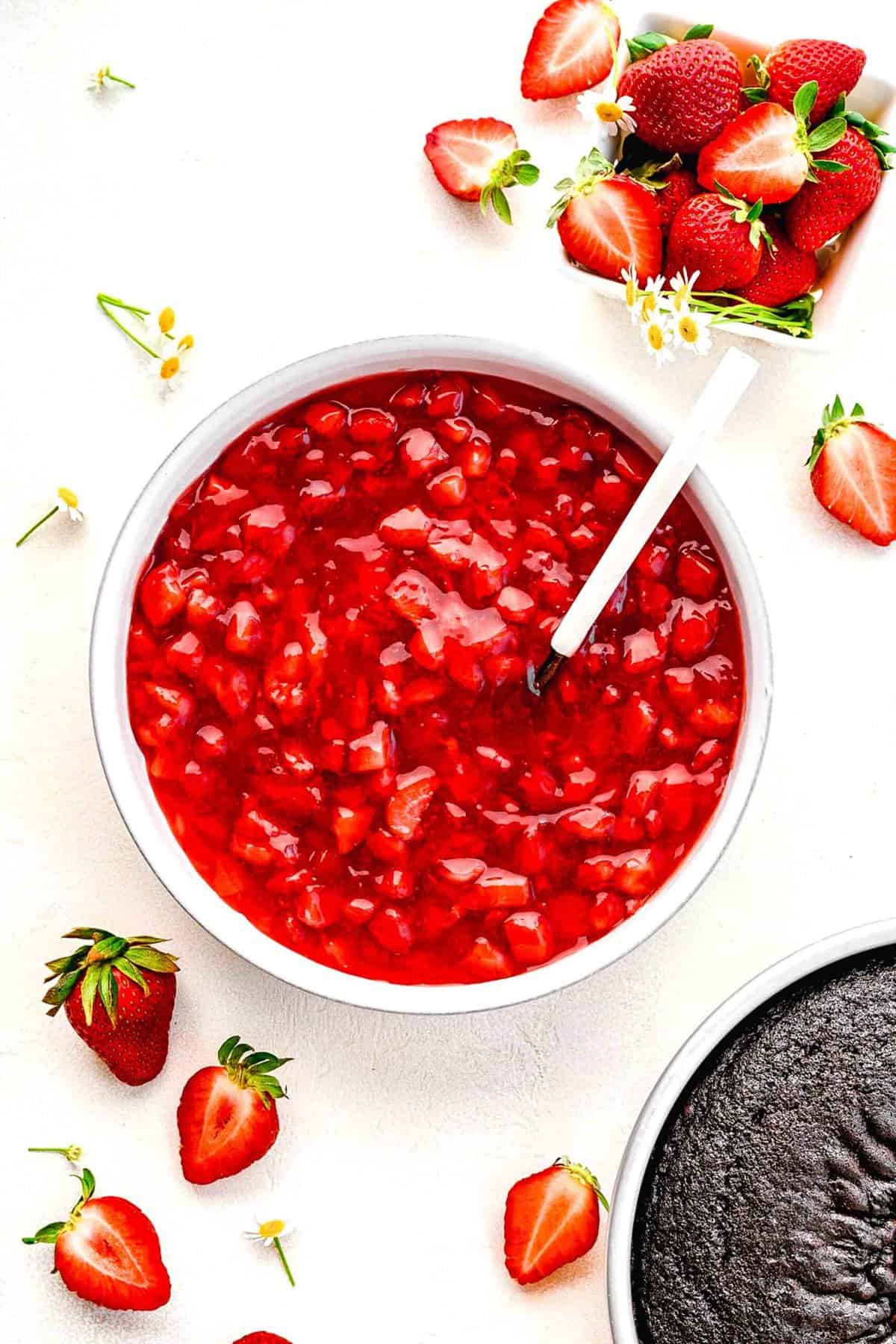 Overhead of strawberry cake filling in a bowl near fresh strawberries.