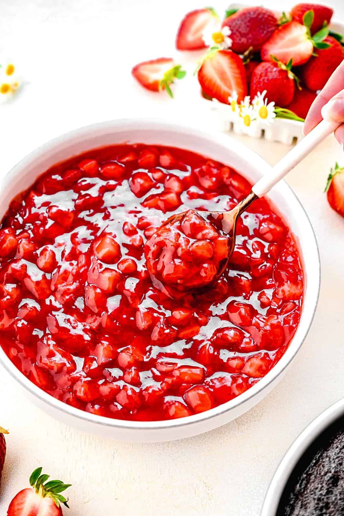 Taking a spoonful out of a bowl of strawberry cake filling near fresh strawberries.