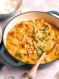 a wooden mixing spoon is placed in a large pot filled with vegetable korma.