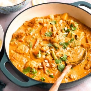 a wooden mixing spoon is placed in a large pot filled with vegetable korma.