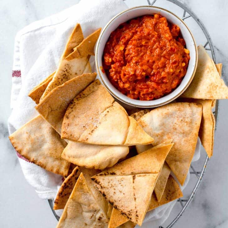 air fried pita bread in a metal basket lined with a linen towel next to a white bowl of red pepper dip