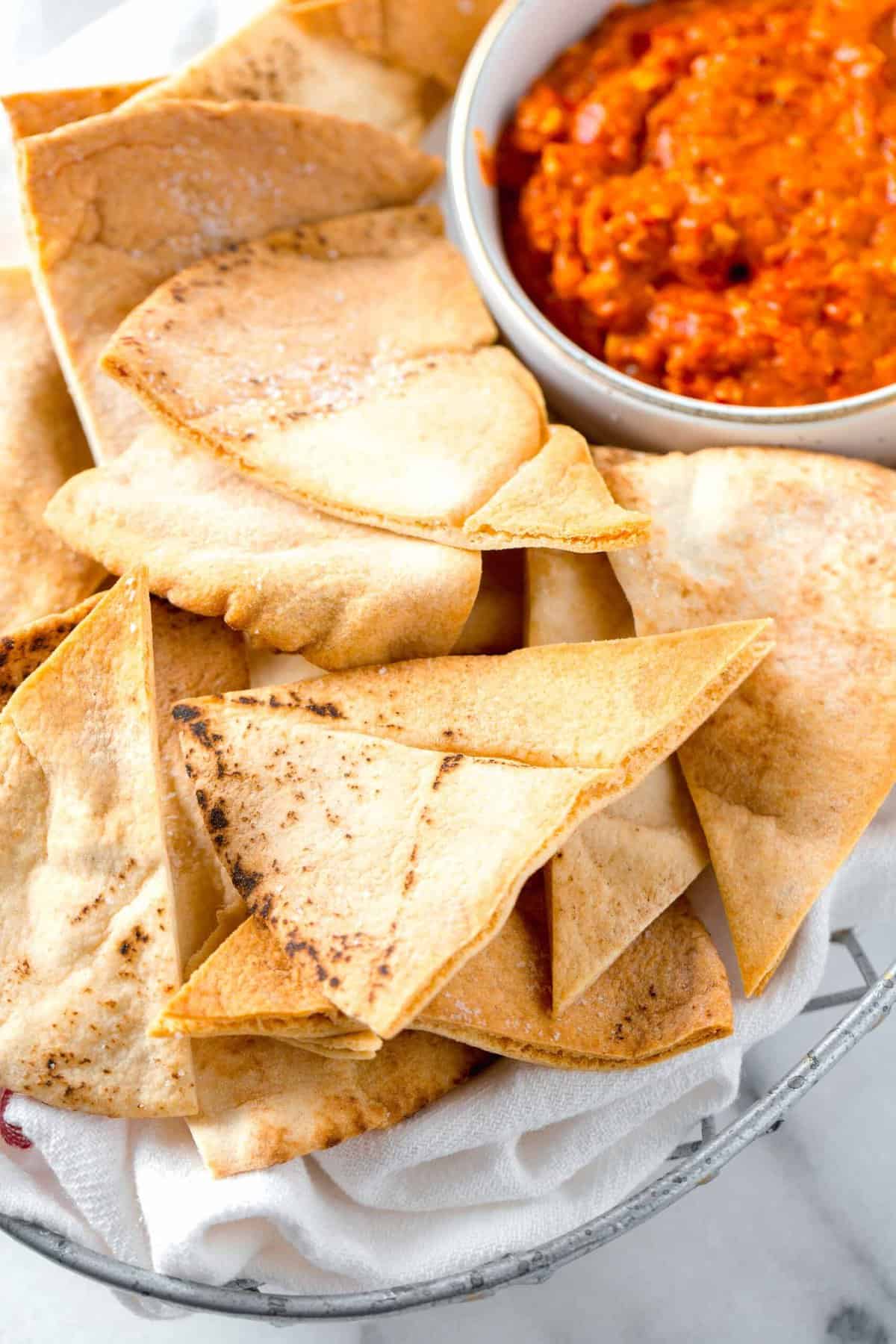 air fried pita chips in a metal basket next to a red pepper dip