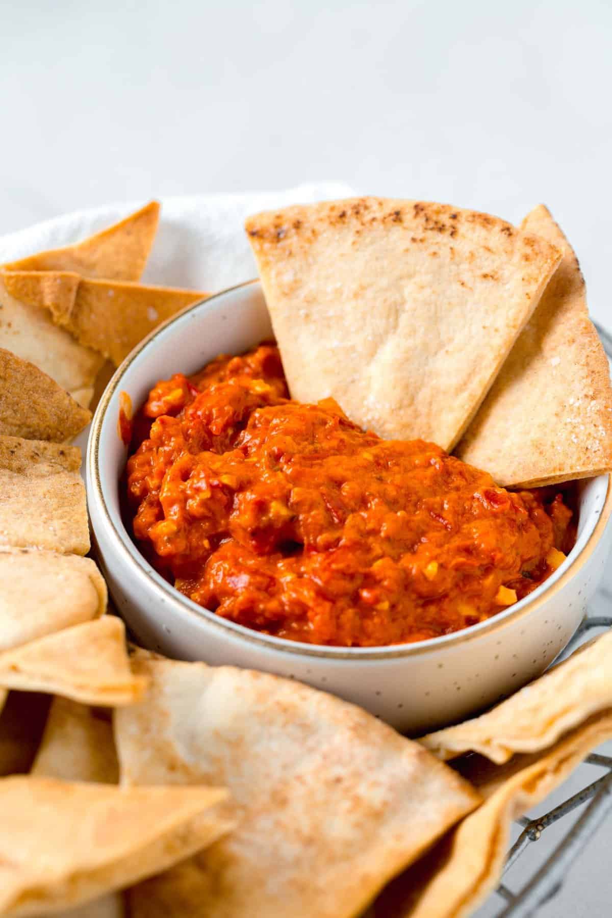 two air fried pita chips sticking out of the red pepper dip in the basket of air fried pita chips