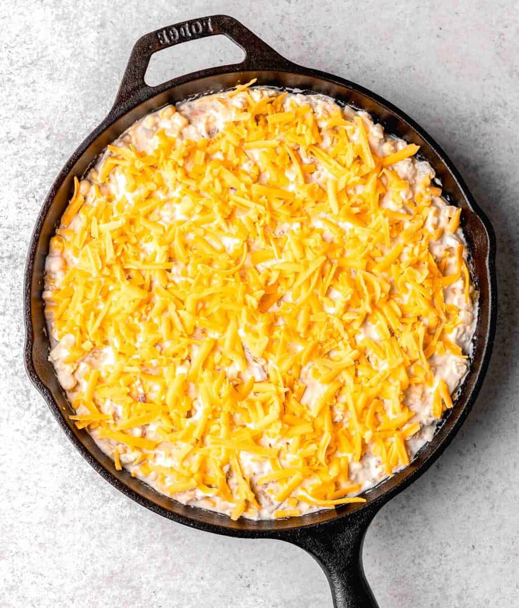 extra shredded cheddar cheese sprinkled on top of the corn dip mixture in the cast iron skillet