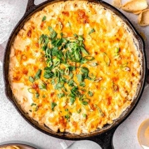 freshly baked corn dip in a cast iron skillet with fresh cilantro and green onions sprinkled on top next to tortilla chips and beer