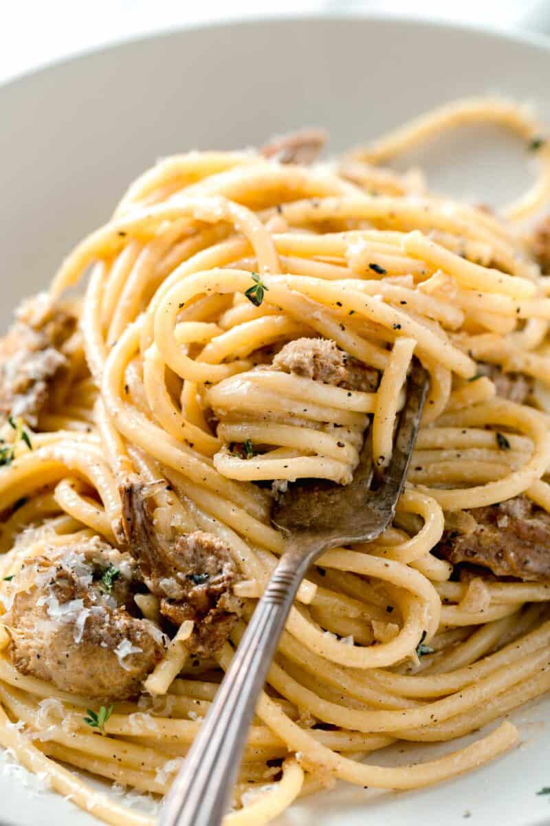 creamy lions mane pasta twisted around a metal fork in a white bowl