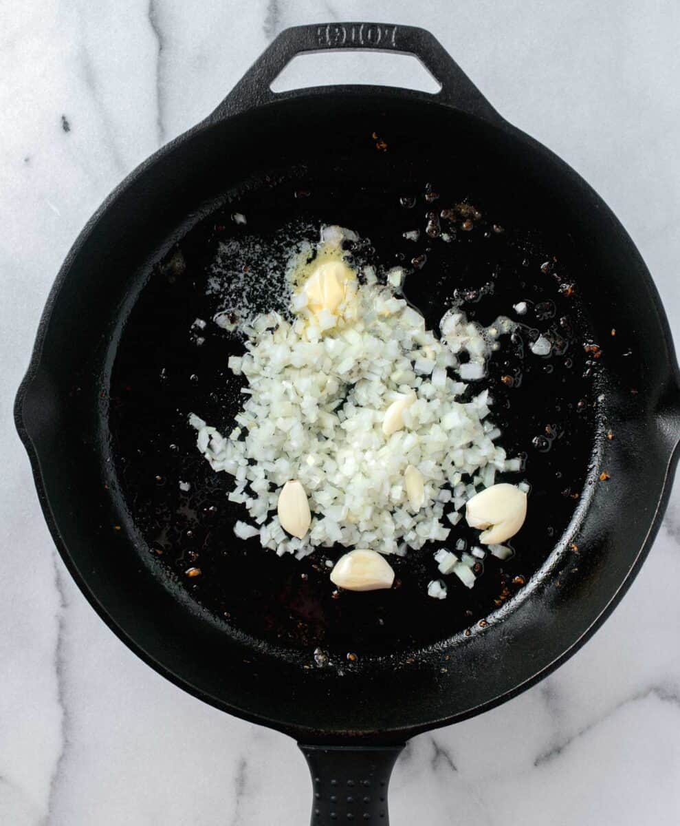 whole, smashed garlic cloves with onion being sautéed in a cast iron skillet with butter