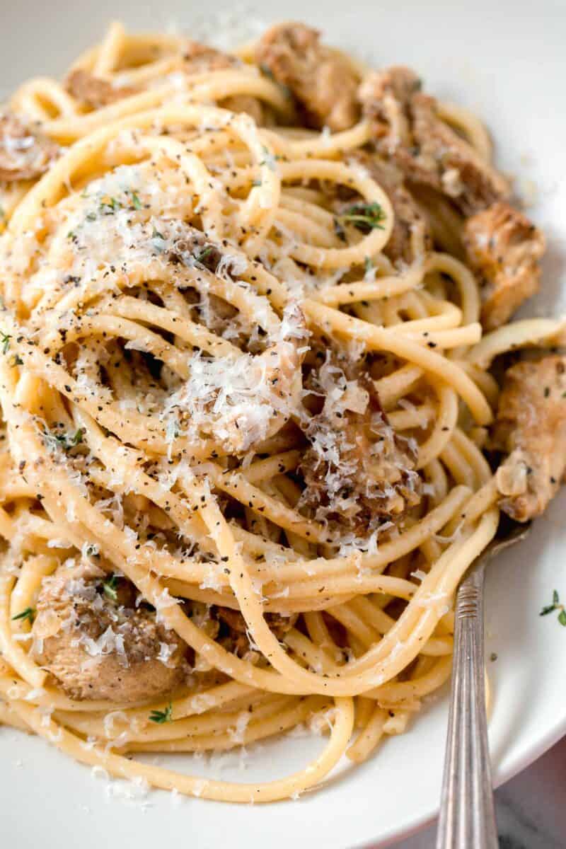 creamy lions mane pasta in a white bowl with a metal fork and fresh parmesan and cracked black pepper sprinkled on top