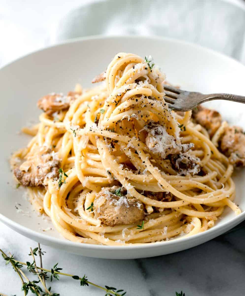 creamy lions mane pasta being lifted out of a white bowl with a metal fork