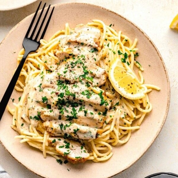 a serving of noodles and chicken is served on a plate with a lemon wedge