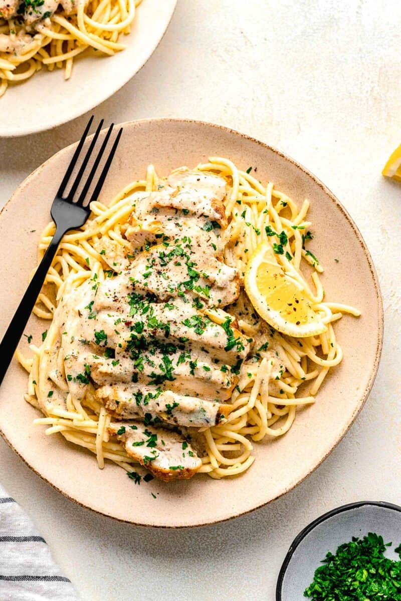 a serving of noodles and chicken is served on a plate with a lemon wedge