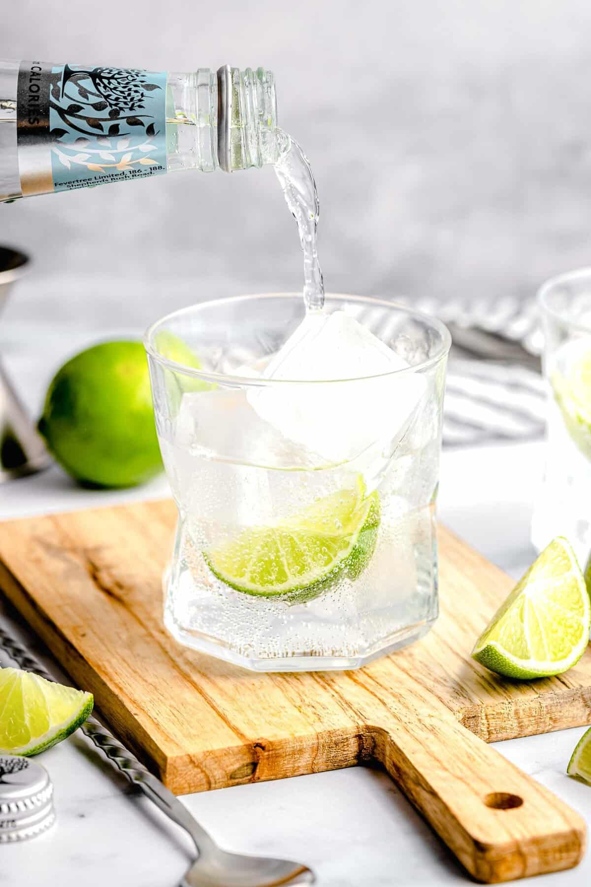 Pouring tonic water over ice and gin in a glass.