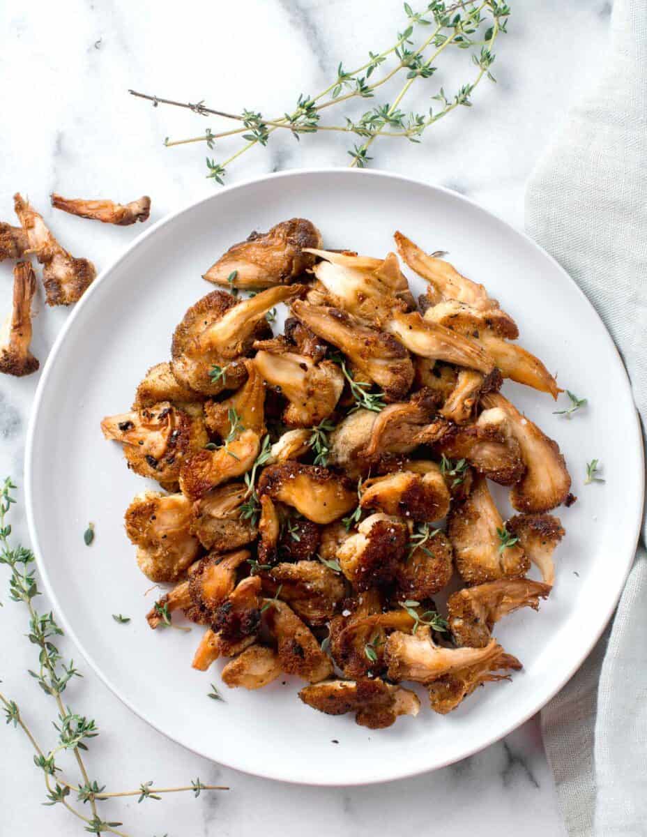 a plate of browned and crispy lion's mane mushrooms with fresh thyme scattered around the plate