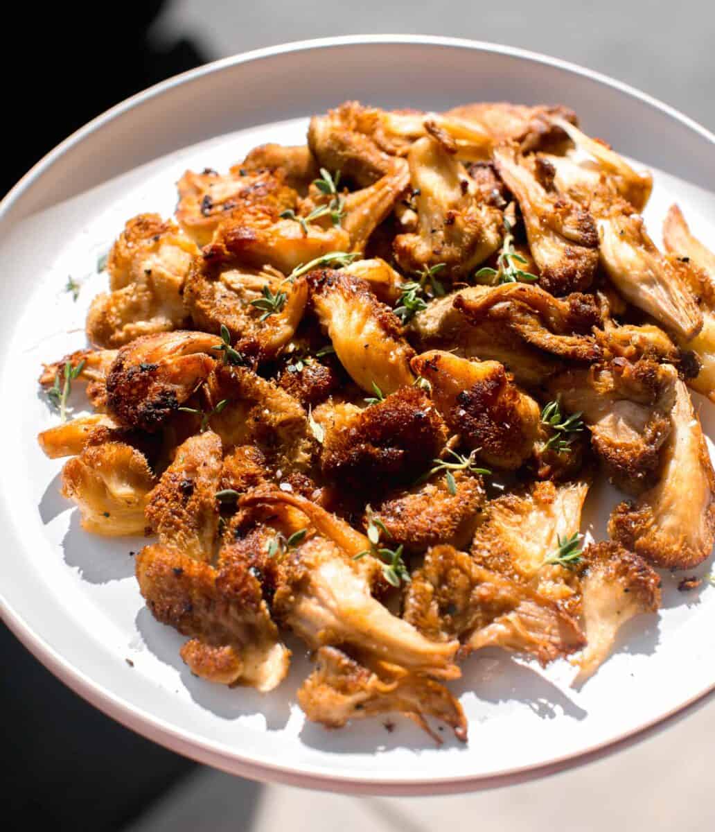 a large plate of cooked lion's mane mushrooms in direct sunlight with fresh thyme on top