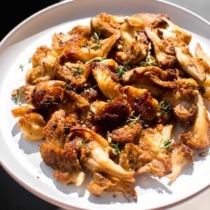 a large plate of cooked lion's mane mushrooms in direct sunlight with fresh thyme on top