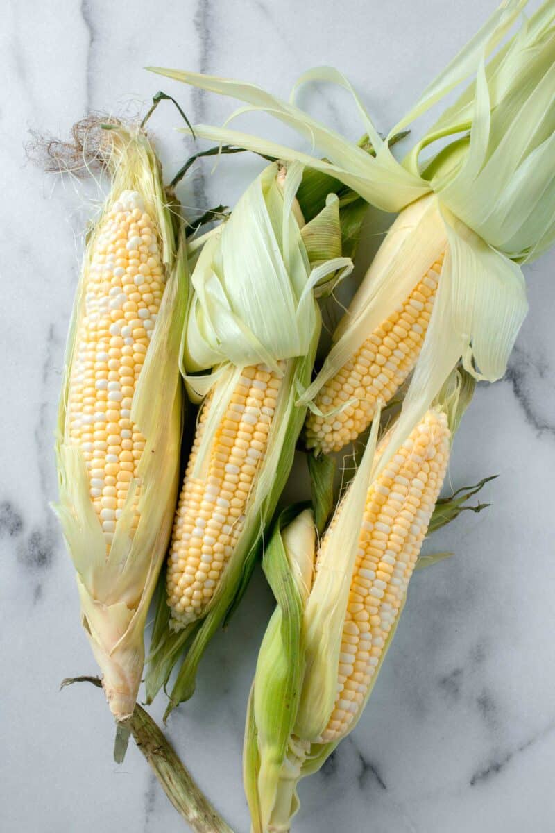 corn in their husks half shucked on a marble countertop