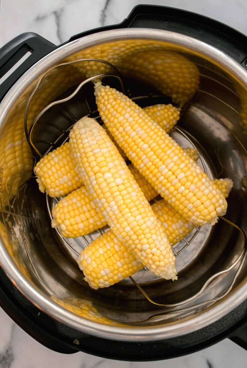 shucked corn stacked on a metal trivet on the inside of an instant pot/pressure cooker