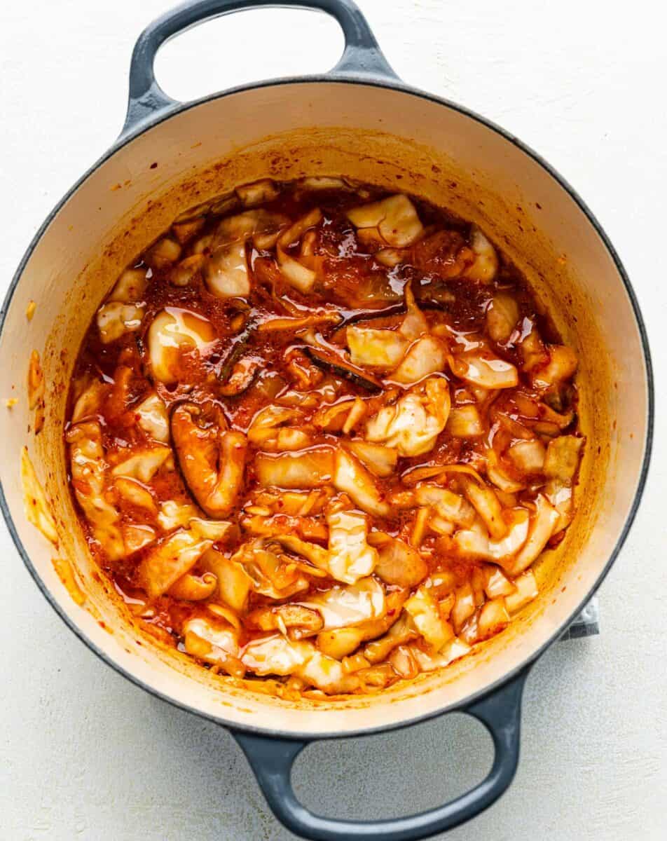 Gochujang paste, kimchi juice, and sautéed mushrooms, kimchi, and garlic in a soup pot.