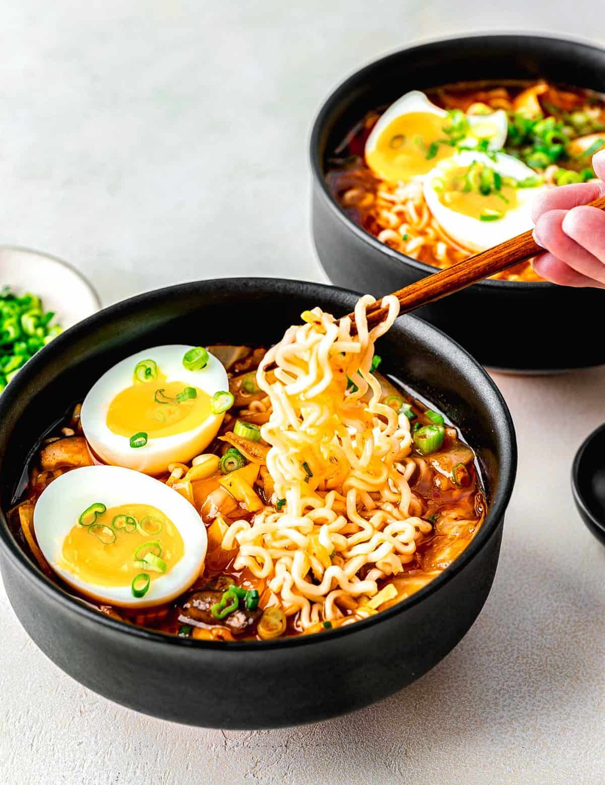 Kimchi ramen served in 2 bowls. A hand with chopsticks is taking a bite out of one of the bowls.