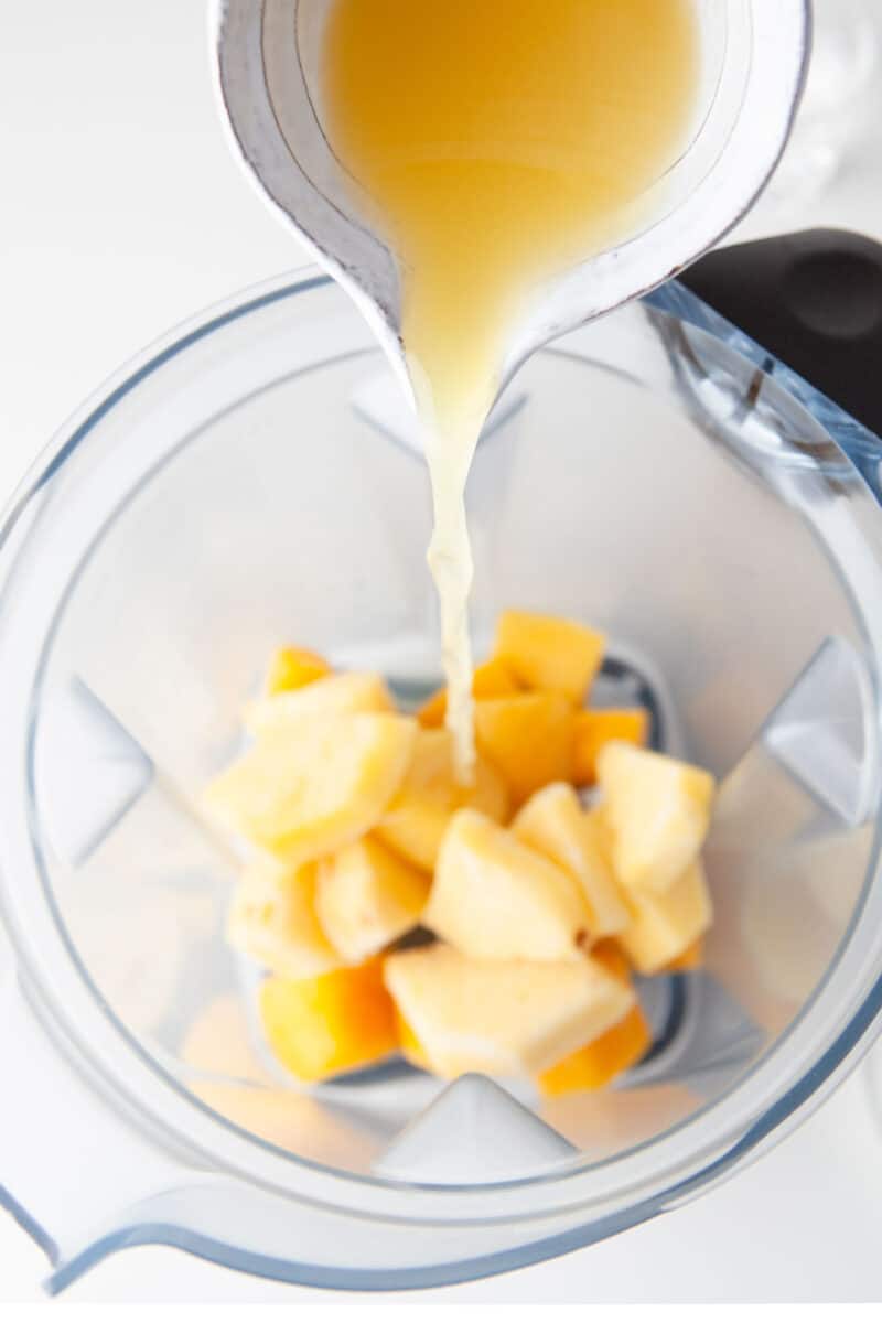 mango chunks are being coated in a liquid in a blender