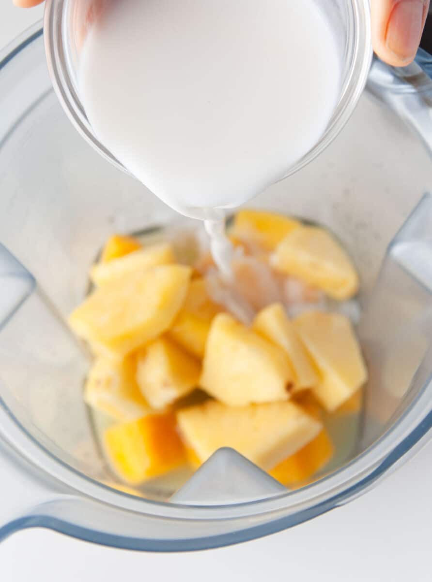 coconut cream is being poured into a blender with mango chunks