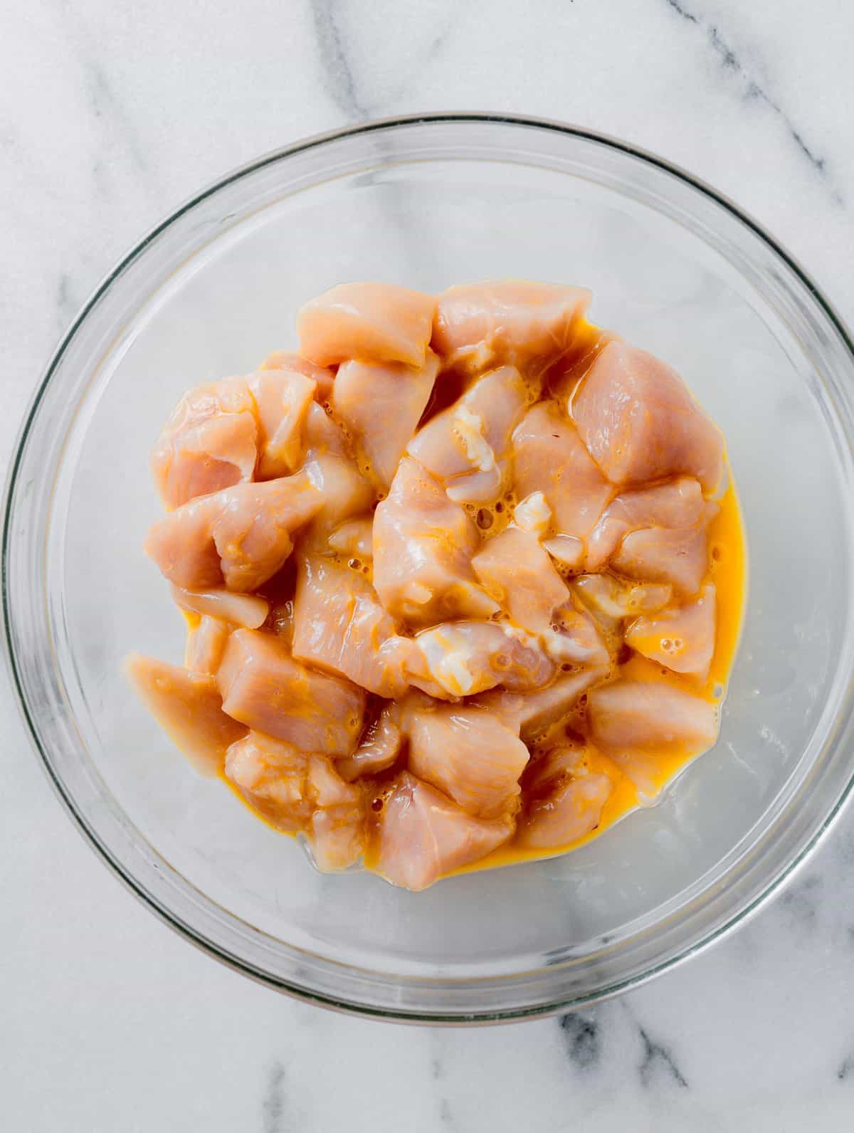 raw chicken cubed and tossed in an egg in a clear bowl