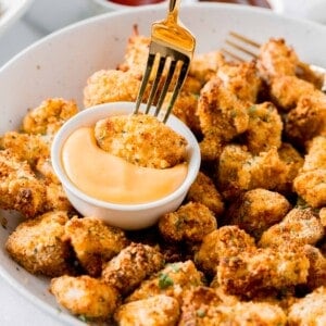 air fried chicken nugget being dipped with a fork in a dipping sauce on a plate of other chicken nuggets