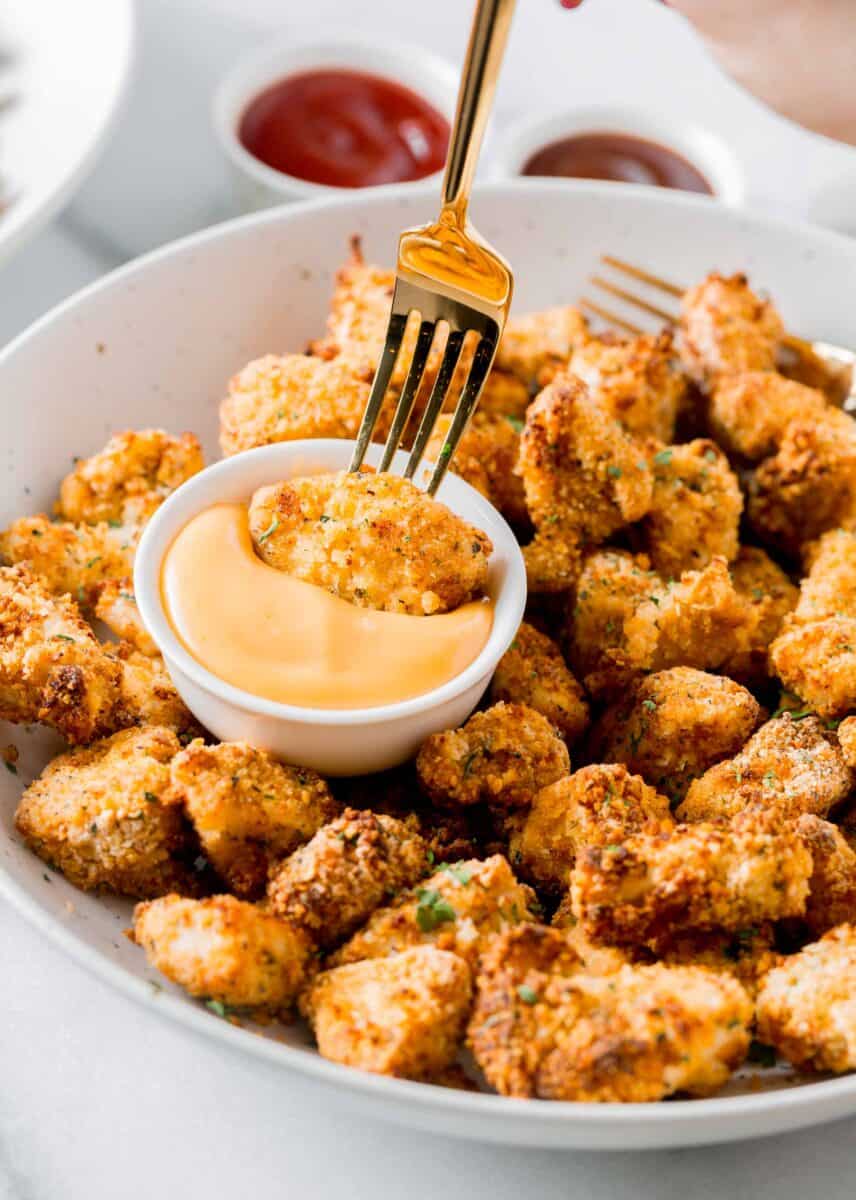 air fried chicken nugget being dipped with a fork in a dipping sauce on a plate of other chicken nuggets