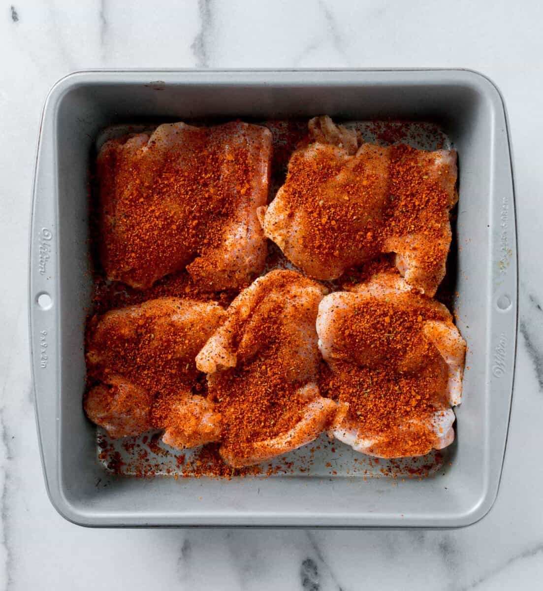 chicken thighs with dry rub sprinkled on top in a metal baking pan