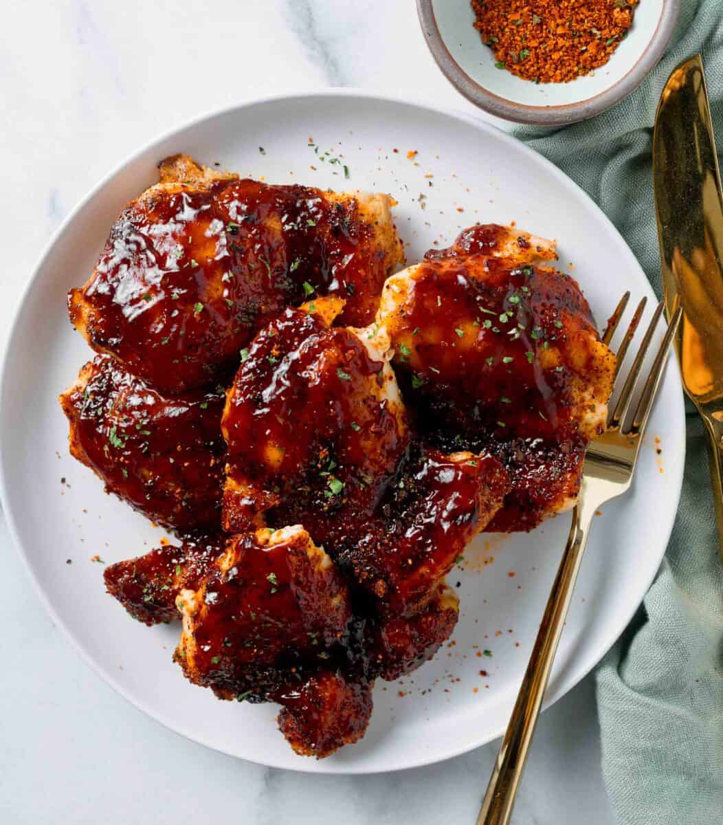 baked bbq chicken thighs with bbq sauce slathered on top next to a gold fork and knife