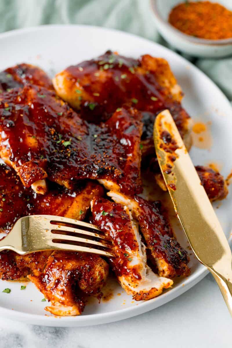 sliced bbq chicken thighs on a white plate with a gold knife and fork