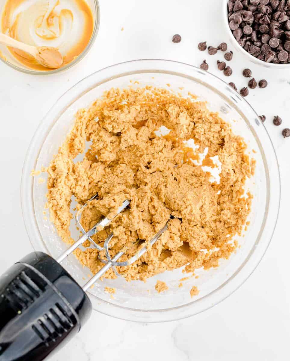 an electric mixer is beating a peanut butter mixture in a glass bowl