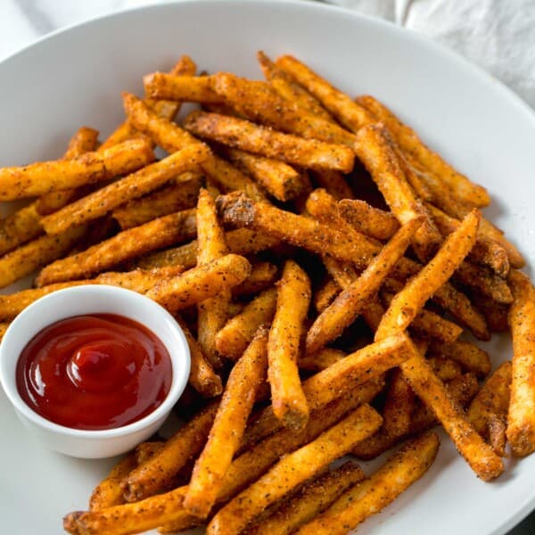 cajun fries in a white bowl next to ketchup