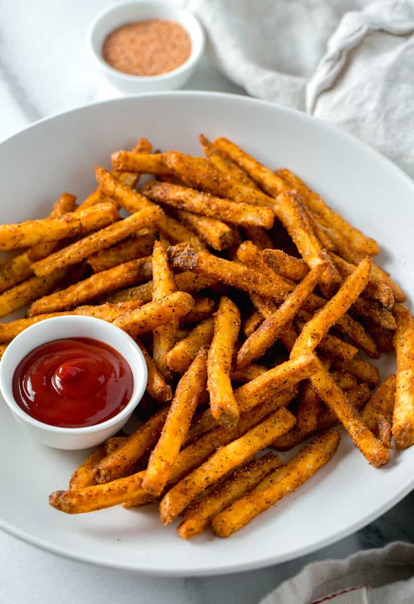 cajun fries in a white bowl next to ketchup