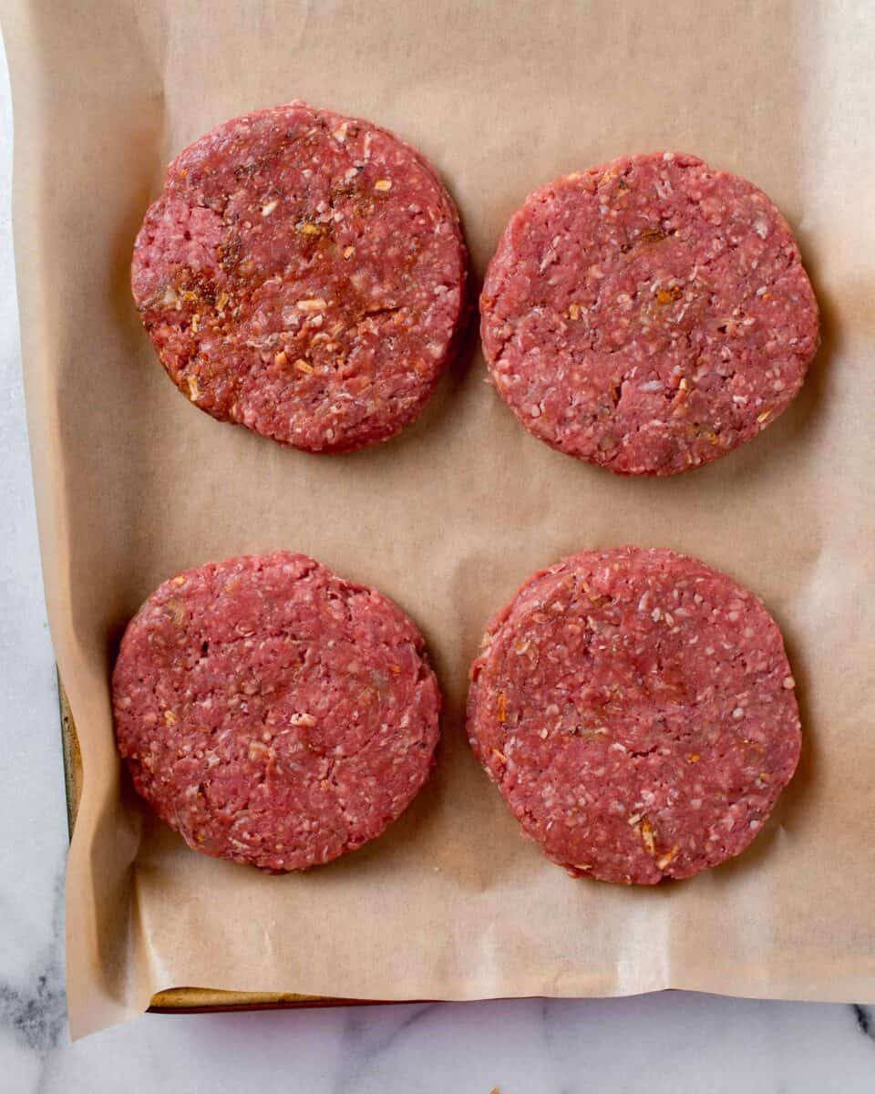 four beef patties formed and placed on a brown piece of parchment paper