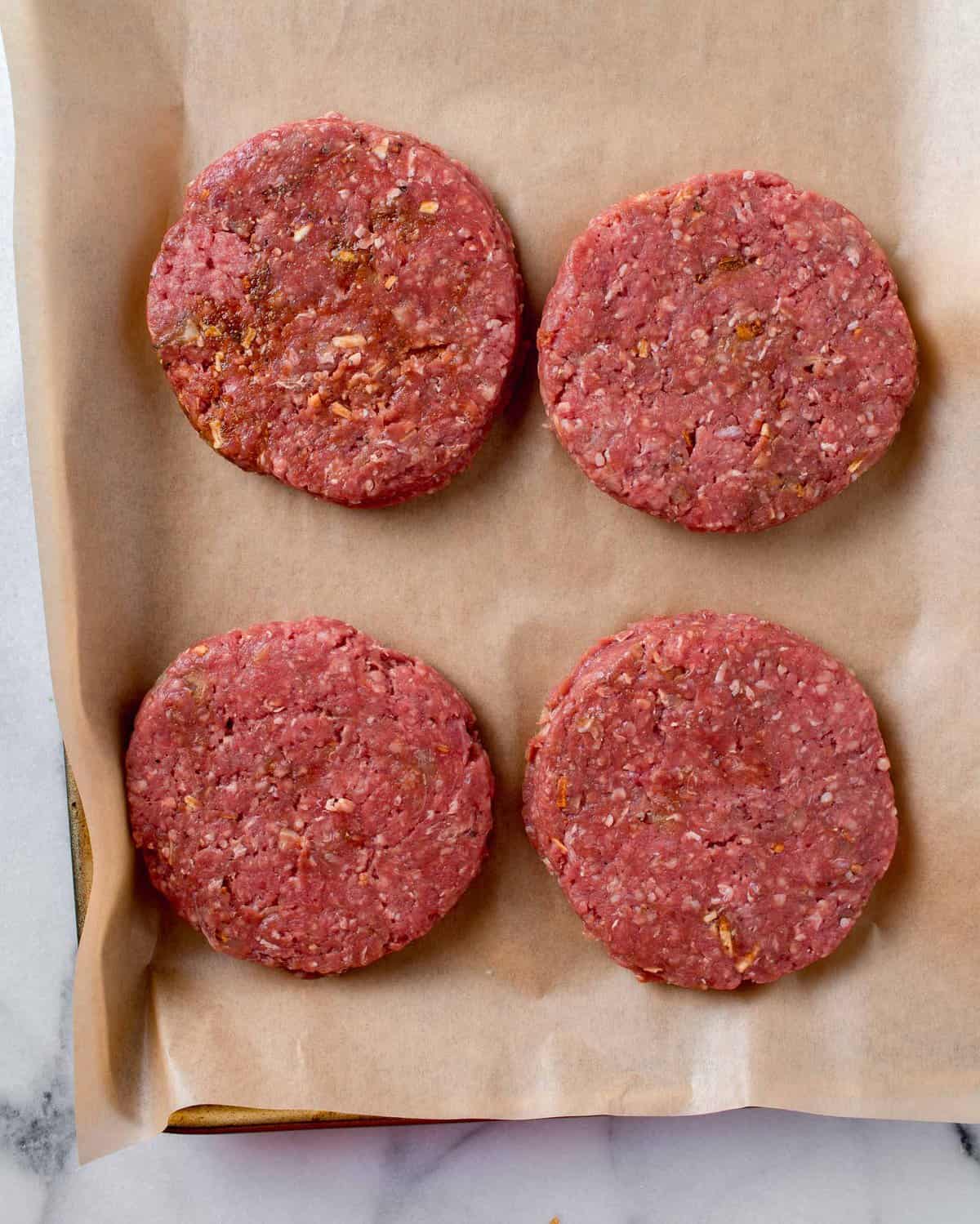 four beef patties formed and placed on a brown piece of parchment paper
