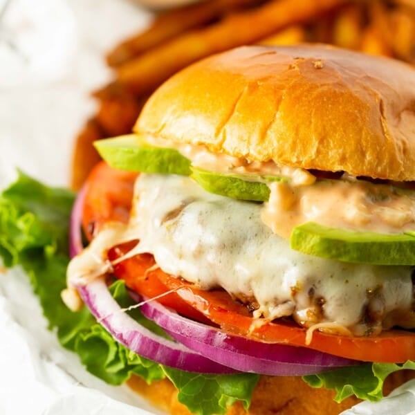 california burger between two brioche buns with burger sauce and avocado on a melted cheese burger patty with tomato, onion, and lettuce.