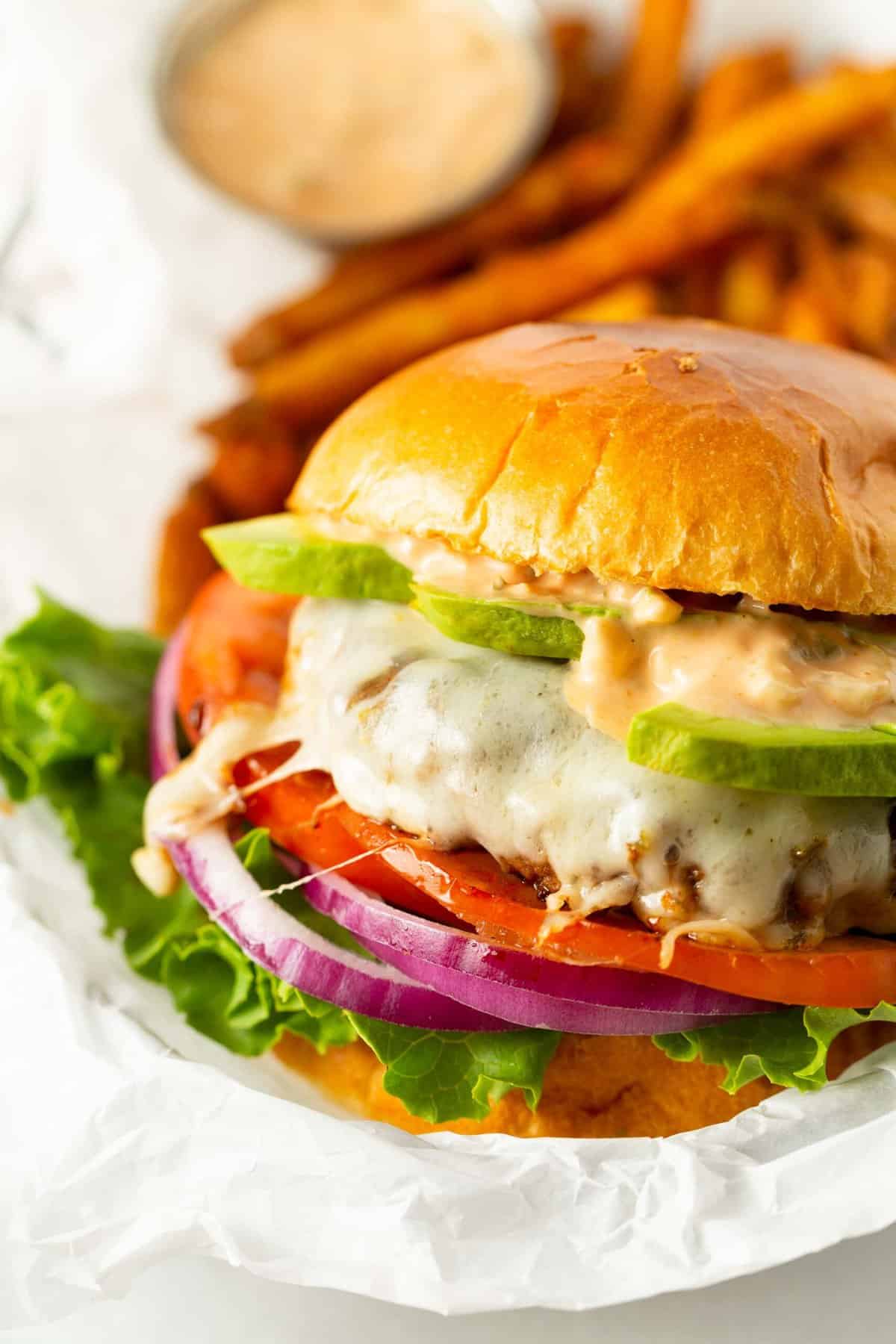 california burger between two brioche buns with burger sauce and avocado on a melted cheese burger patty with tomato, onion, and lettuce.