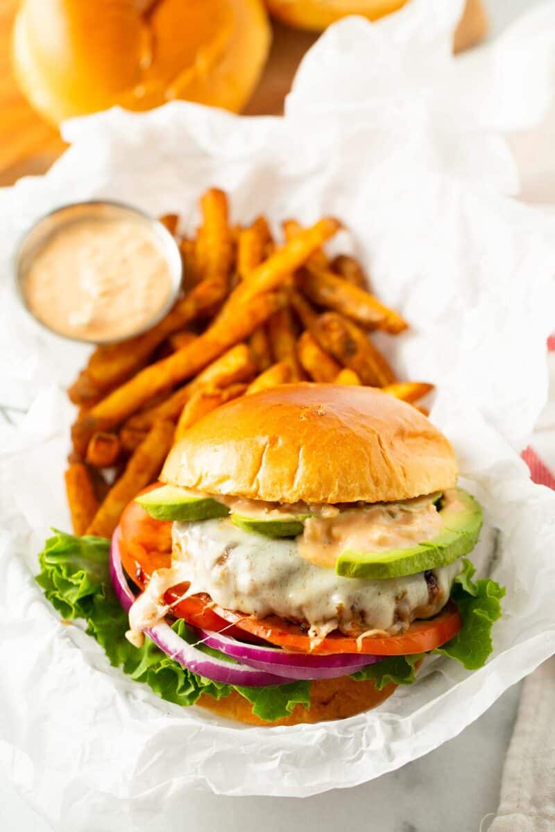 california burger in a basket lined with white parchment paper along with french fries and a condiment container